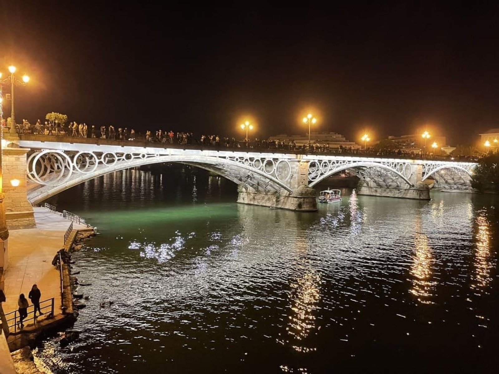 Puente de Triana iluminado y reflejado en el río Guadalquivir